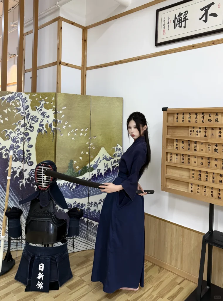 来访者在日新馆浪花屏风与护具展示旁持剑站立留影